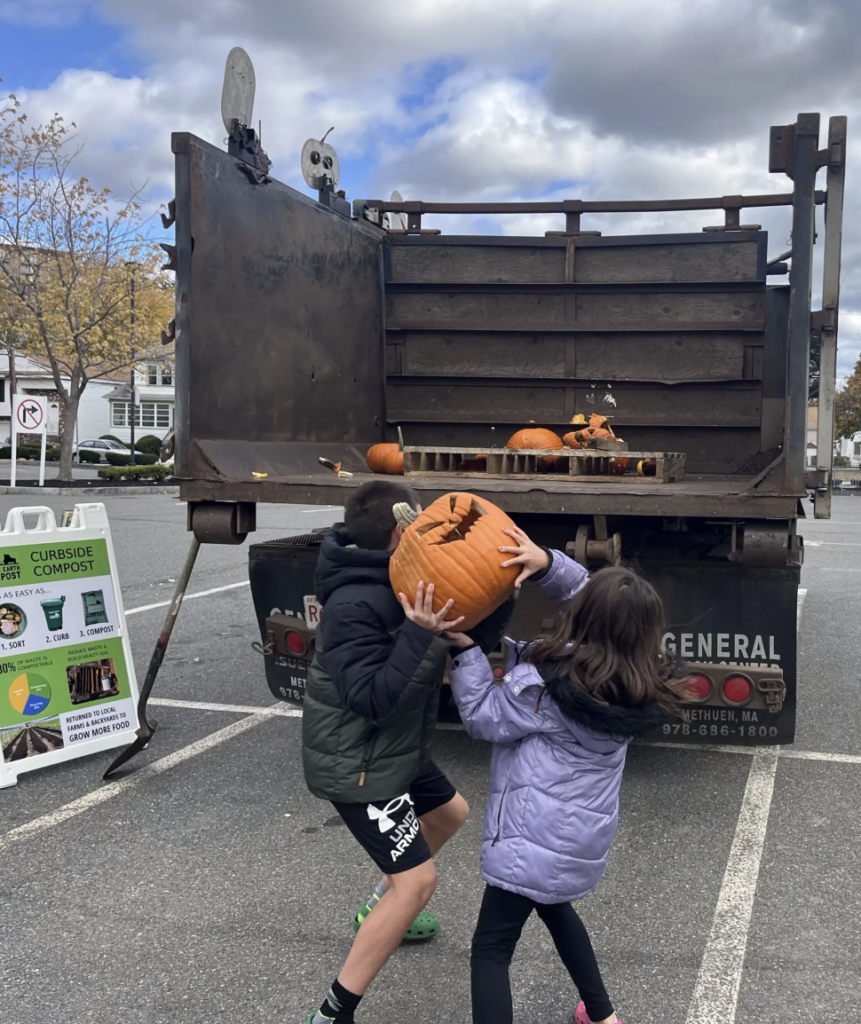 Two kids throw a jack 'o lantern into a compost truck