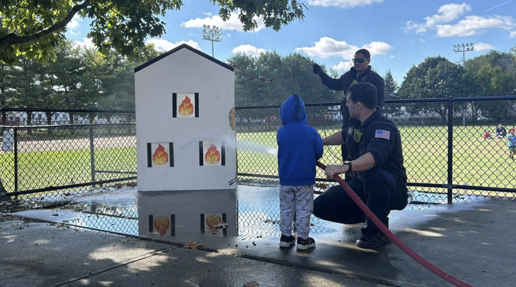 A police officer helps a child "extinguish" a pretend house on fire