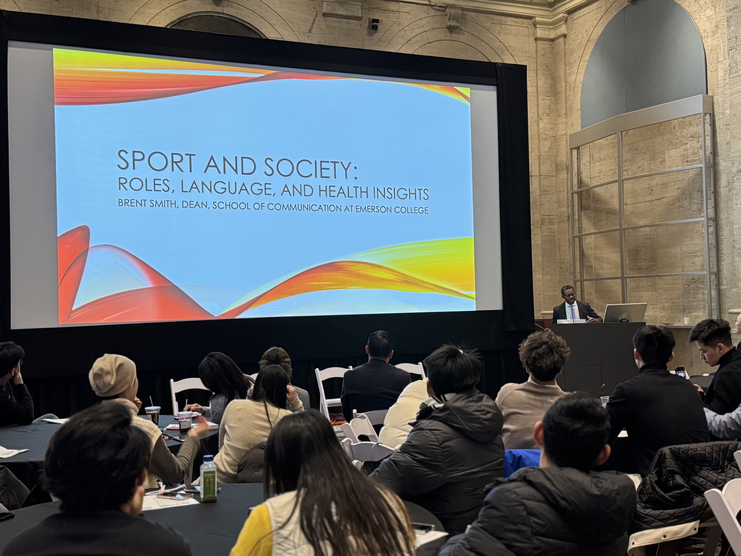 Standing behind a podium presenting to a roomful in Bordy Theater, Dean Brent Smith of Emerson’s School of Communication explores the role of language in shaping athletes' well-being. [Photo/Molly Loughman]