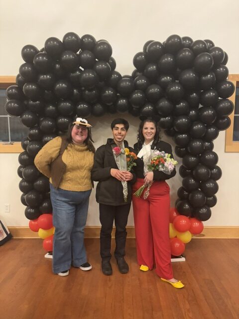 Three people stand together with a balloon arch shaper like Mickey Mouse ears.