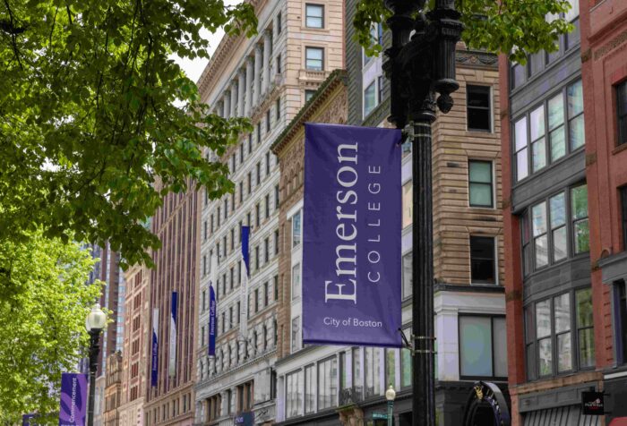 Purple banners with the words "Emerson College, City of Boston" hang from street lights, with buildings in the background.