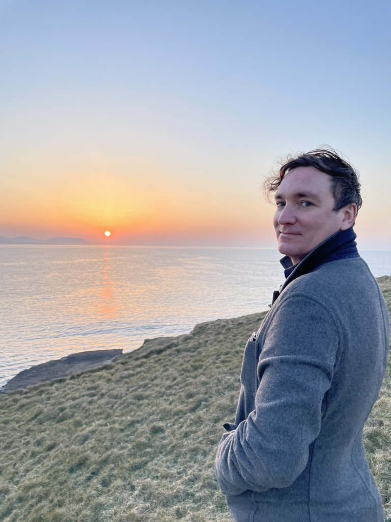 Hunter Vaughan stands outside in Ireland while the sunsets over water