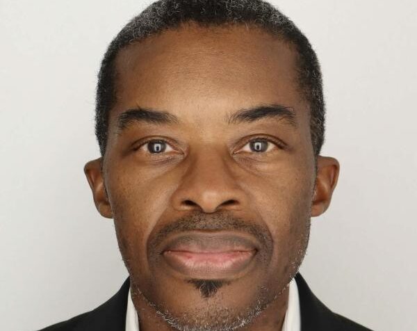 A man wearing a black suit coat smiles for a photo.