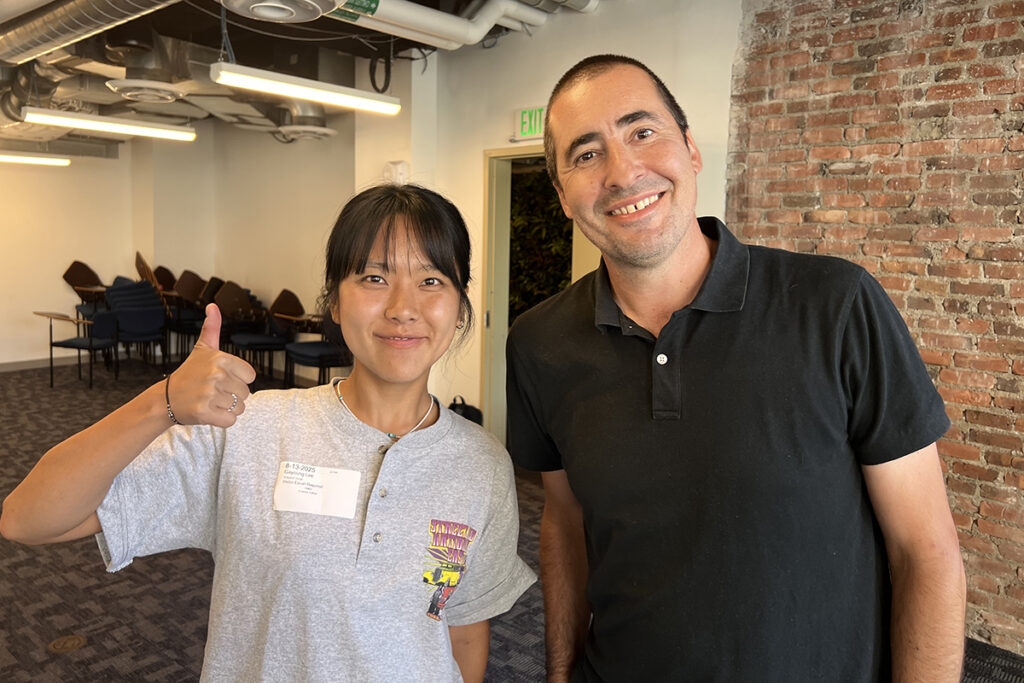Man in black polo shirt stands with student in grey T-shirt giving thumbs up