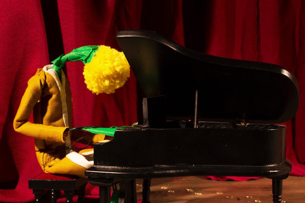 A stop-animation still of what looks like a dandelion wearing an outfit while playing a piano