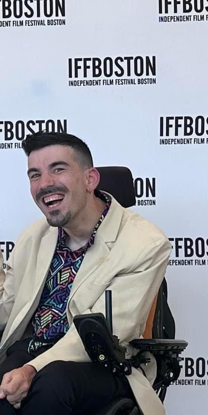 Alexander Freeman smiling while sitting in a wheelchair with a film festival backdrop