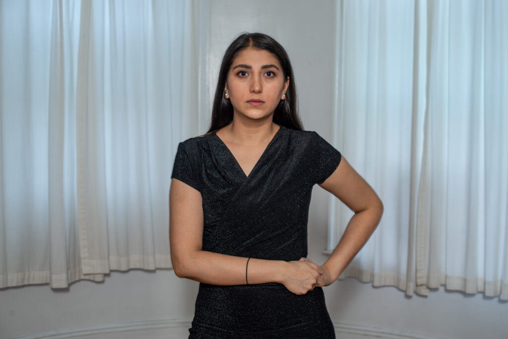 A person wearing a dress poses for a photo, both arms on one hip.