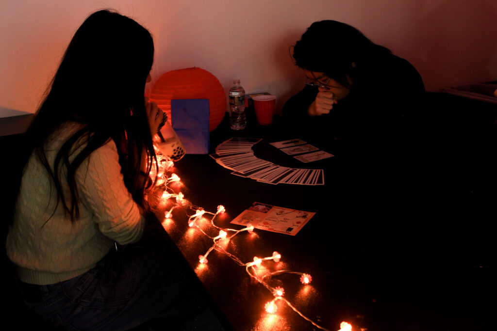 Two students in a dark area with lit candles play with tarot cards