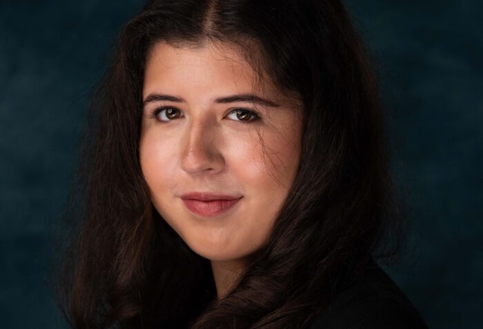 A person smiles for a portrait against a dark background.