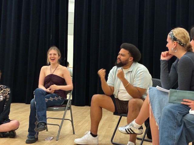 Kai Tshikosi talks while sitting in a seat with people around him.
