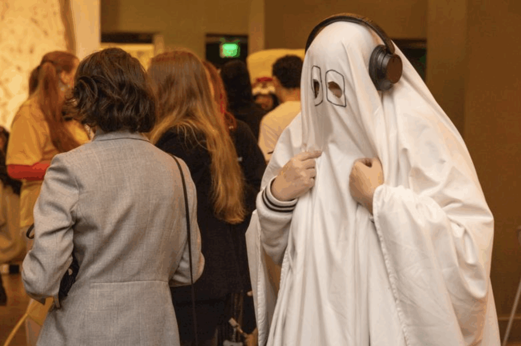 A person wearing a sheet as a ghost costume with headphones on their head
