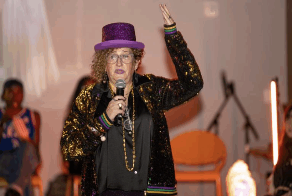 A woman dressed with a purple hat raises her hand while talking
