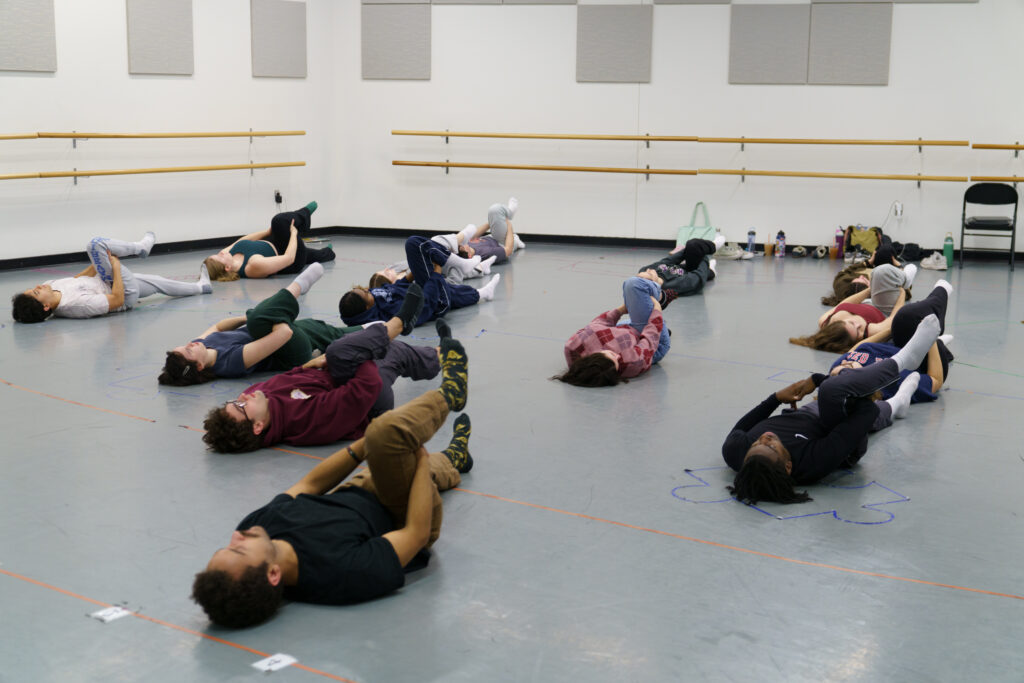 Student lay on their backs with one leg in the air as they hold onto that leg's calf