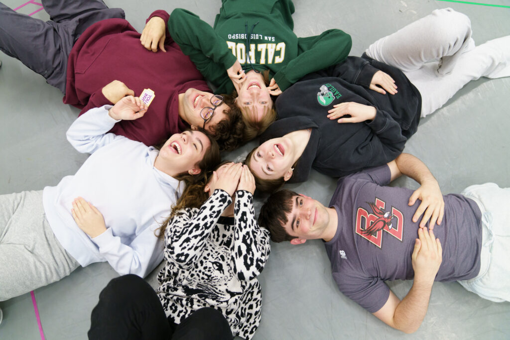 Six students lay on the ground with their heads against each other during a classroom exercise.