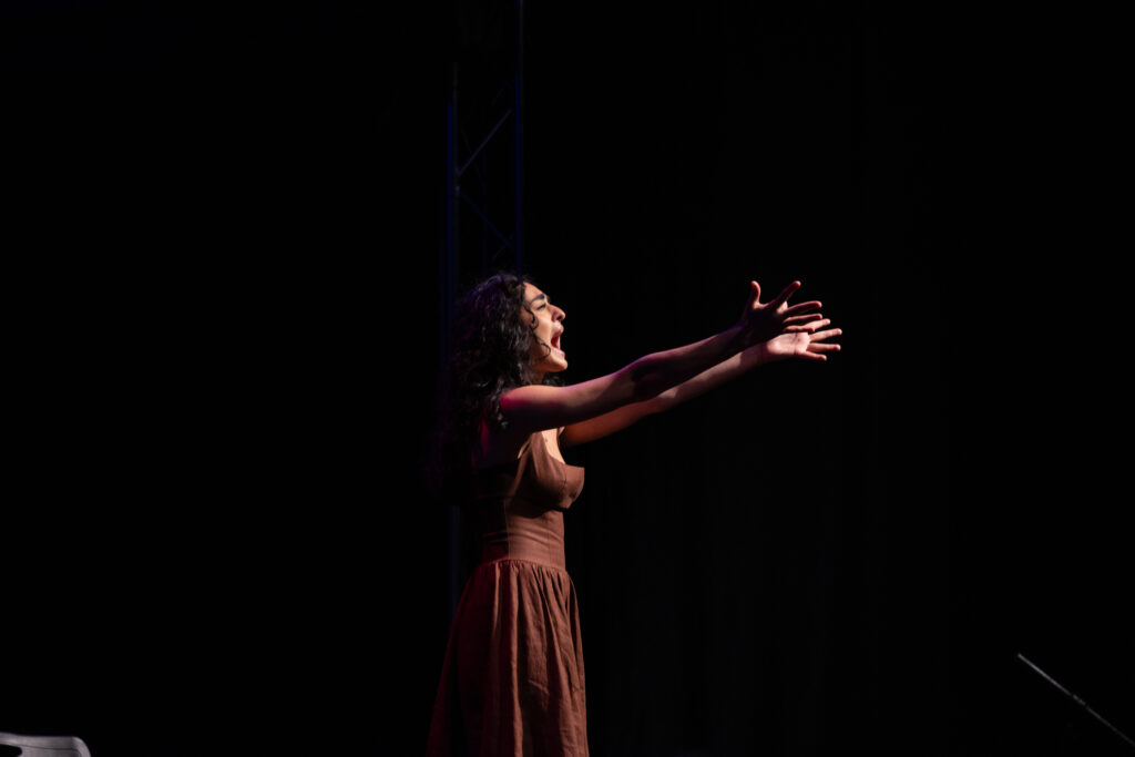 A person reaches out while they sing or speak on stage