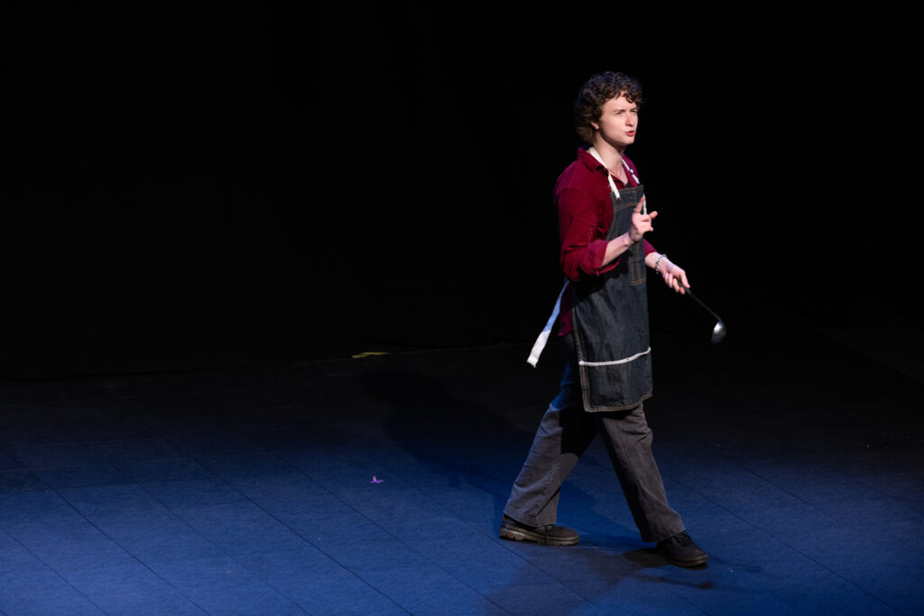 A person wearing an apron walks and sings or talks while on stage