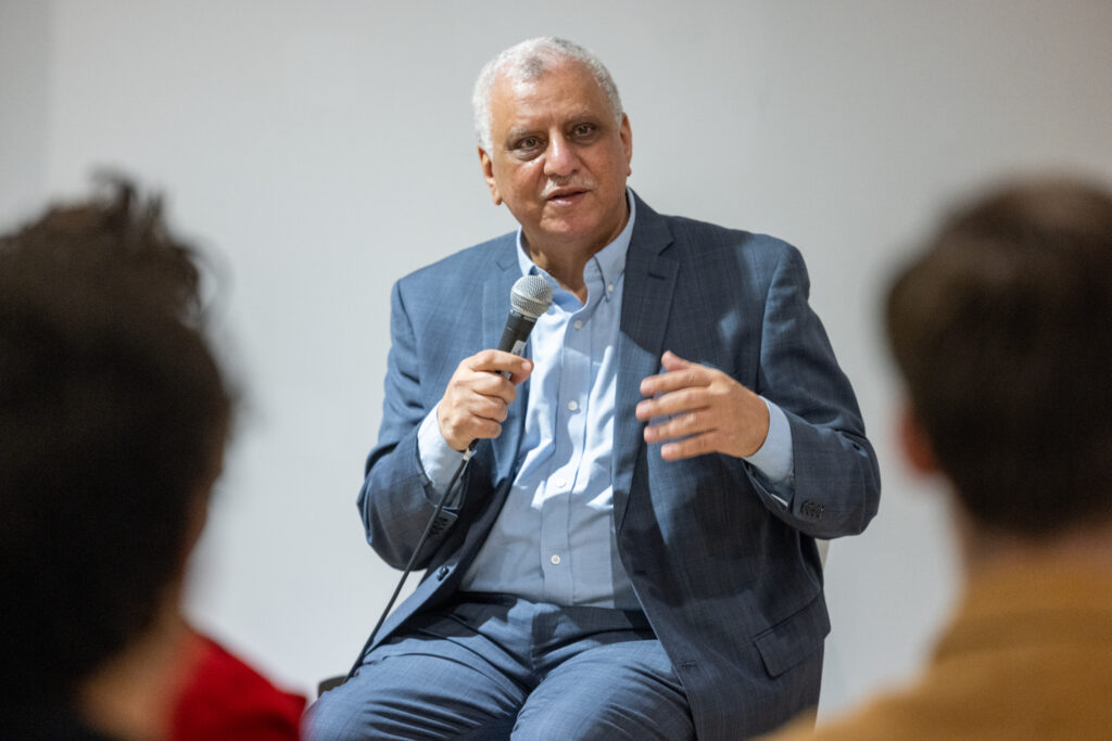 Mohamed Khalil talks an audience while sitting on a stool and holding a microphone
