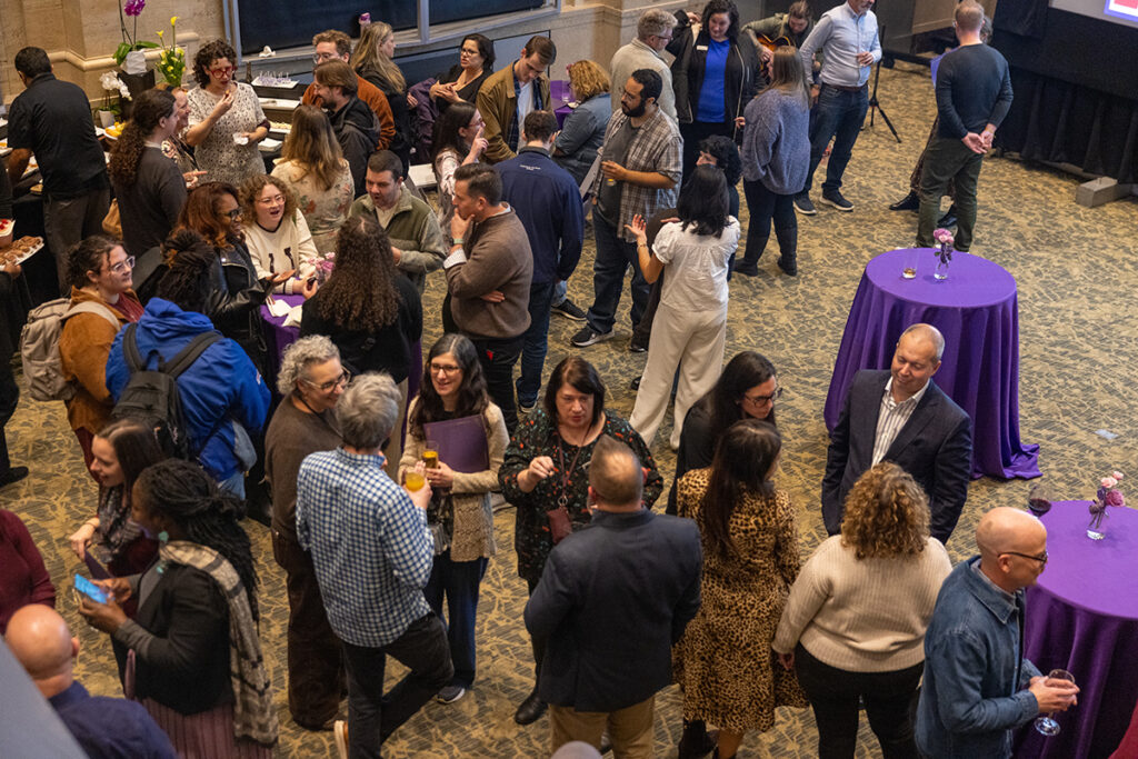 crowd stands around drinking, talking amongst cocktail tables