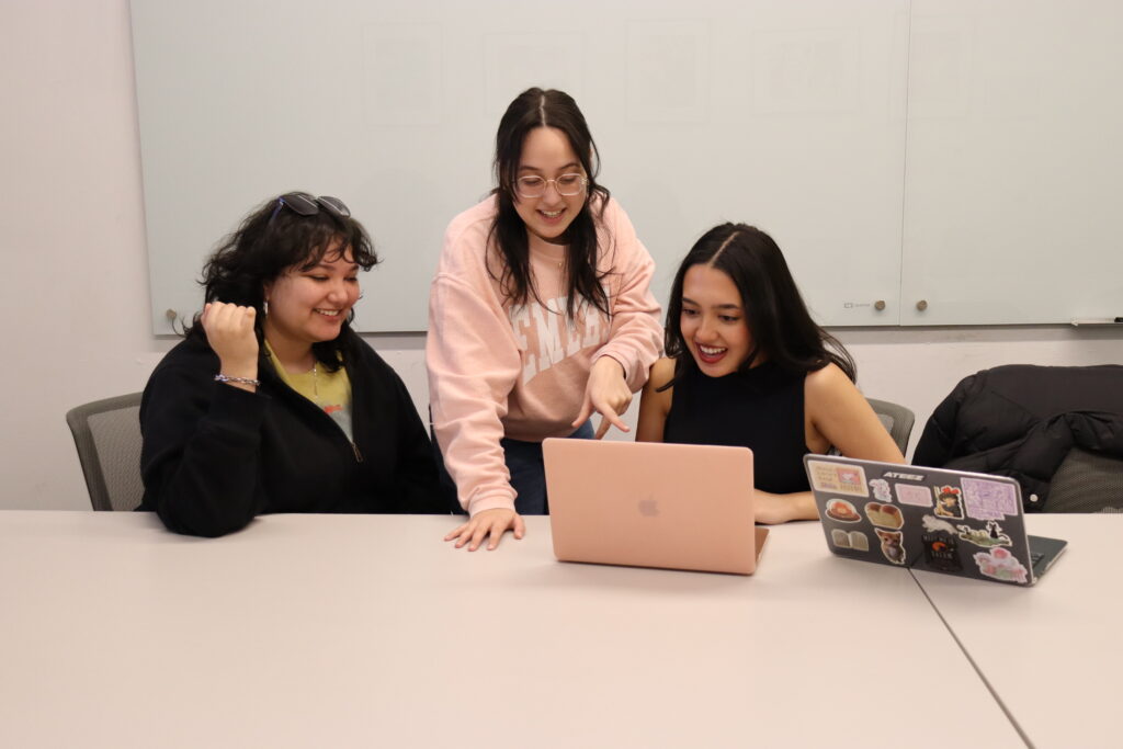 Christina Sanchez, Aylin Isik, Elani Waight sit and stand around a laptoop