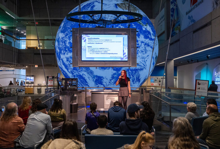 A person speaks on stage in front of a large screen with a giant globe behind them