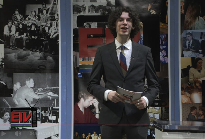 Noah Berkowitz speaks to the camera while standing and holding cue cards