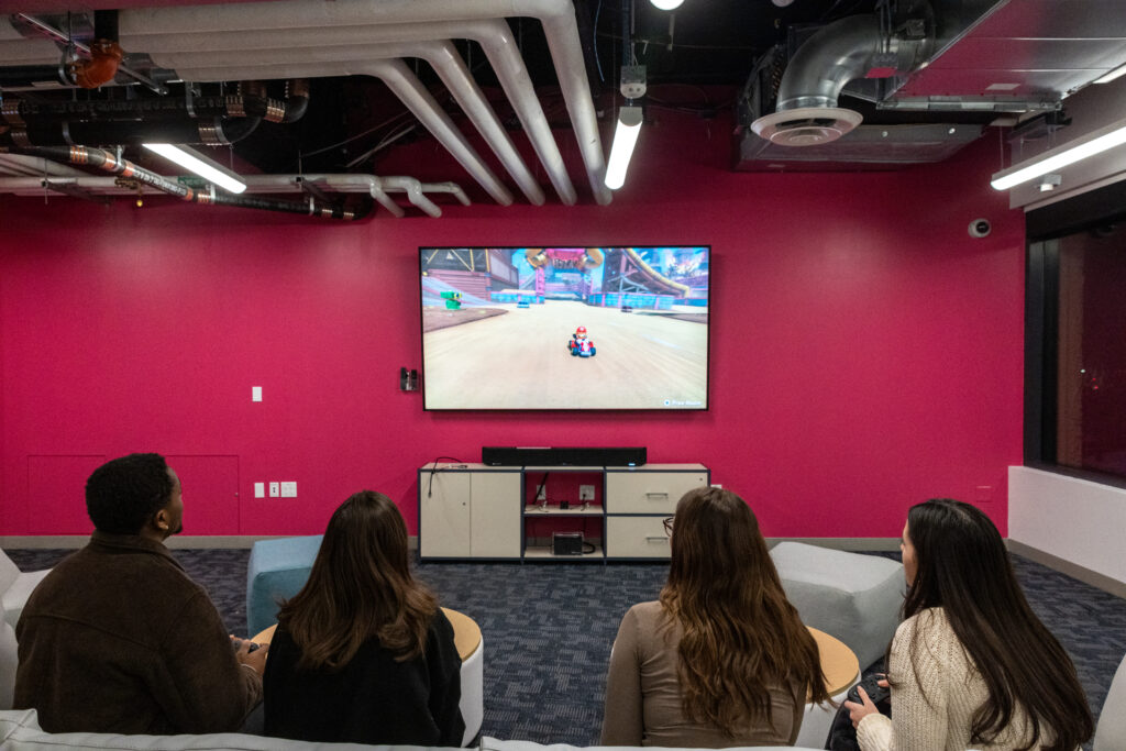 Over the shoulder photo of people playing Switch while looking at a TV screen