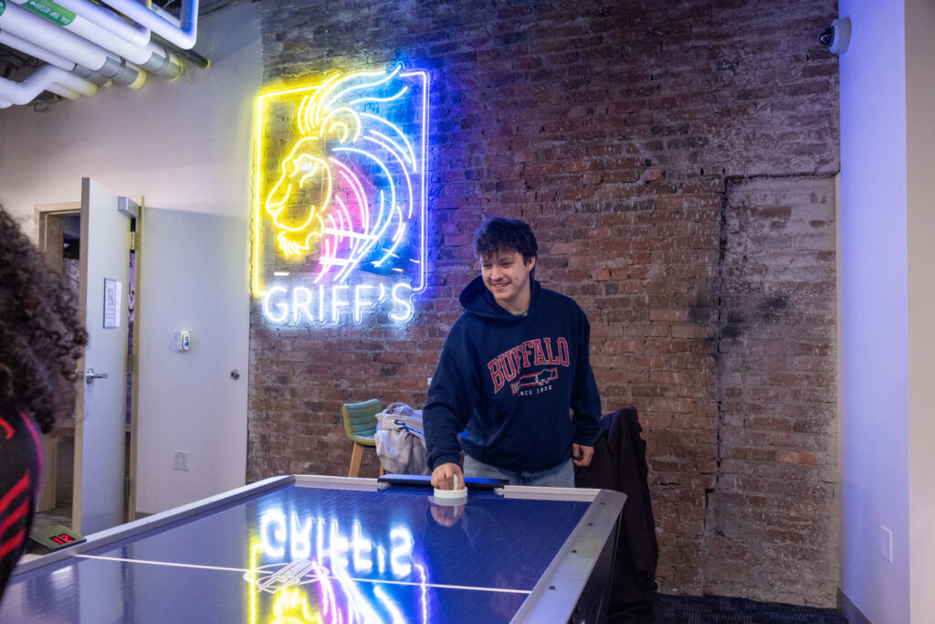 A person plays air hockey with the neon Griff's Room sign in the background on the wall.