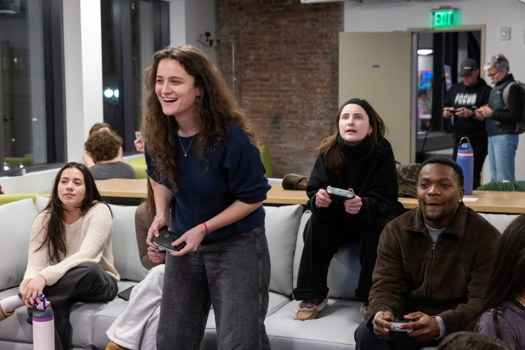 A person stands with a Switch controller while others sit on a couch withe game controllers