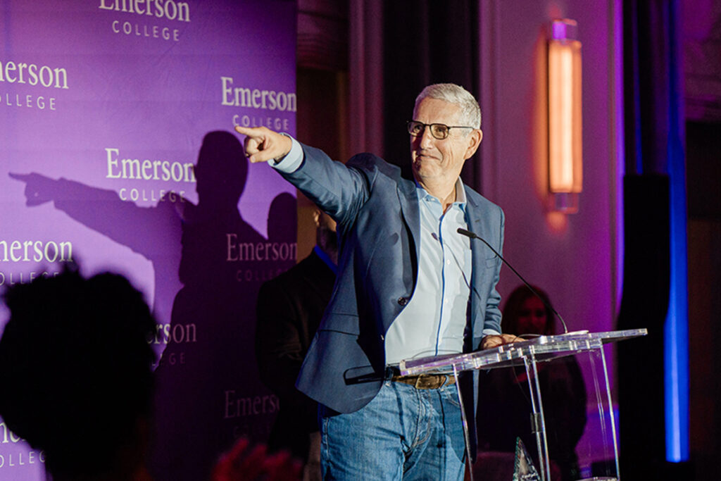 Doug Herzog in blue blazer points off camera behind podium in front of Emerson branded backdrop