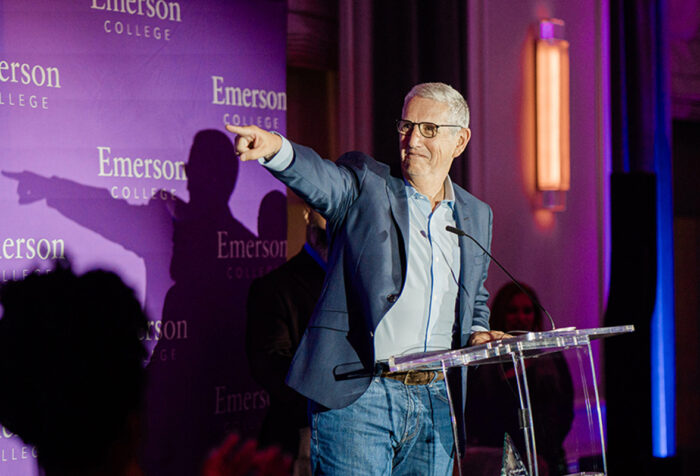 Doug Herzog in blue blazer points off camera behind podium in front of Emerson branded backdrop