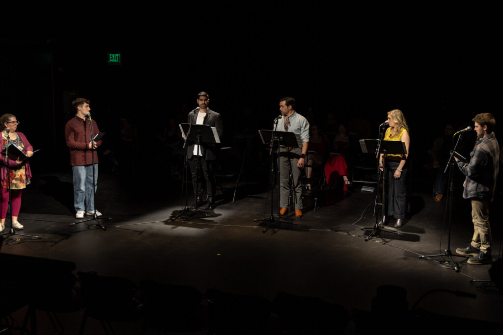 Five performers with spotlights on them with darkness around them