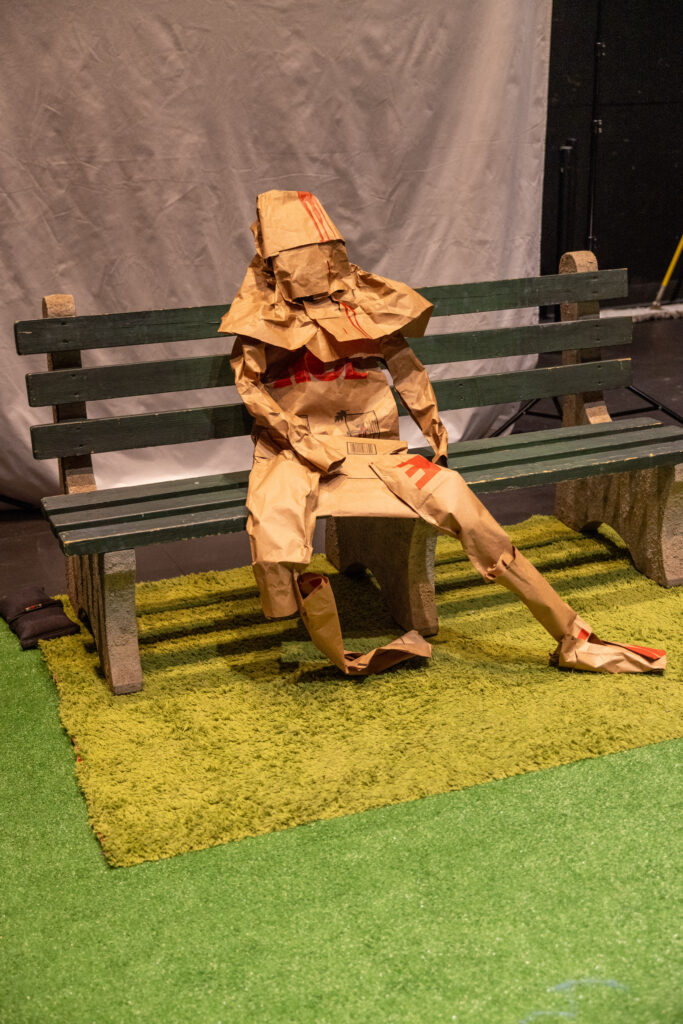 A person is cloaked in paper bags while sitting on a park bench