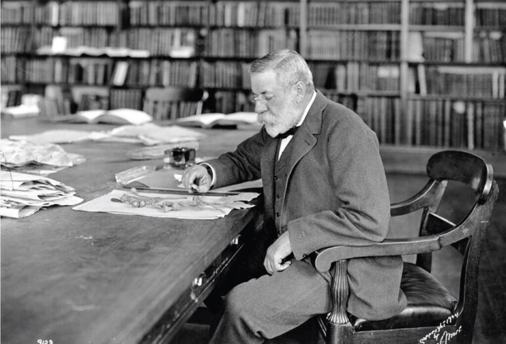 Man in 19th century dress looks at a plant on a library table