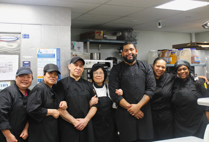 Kitchen workers in black shirts, pants stand in kitchen