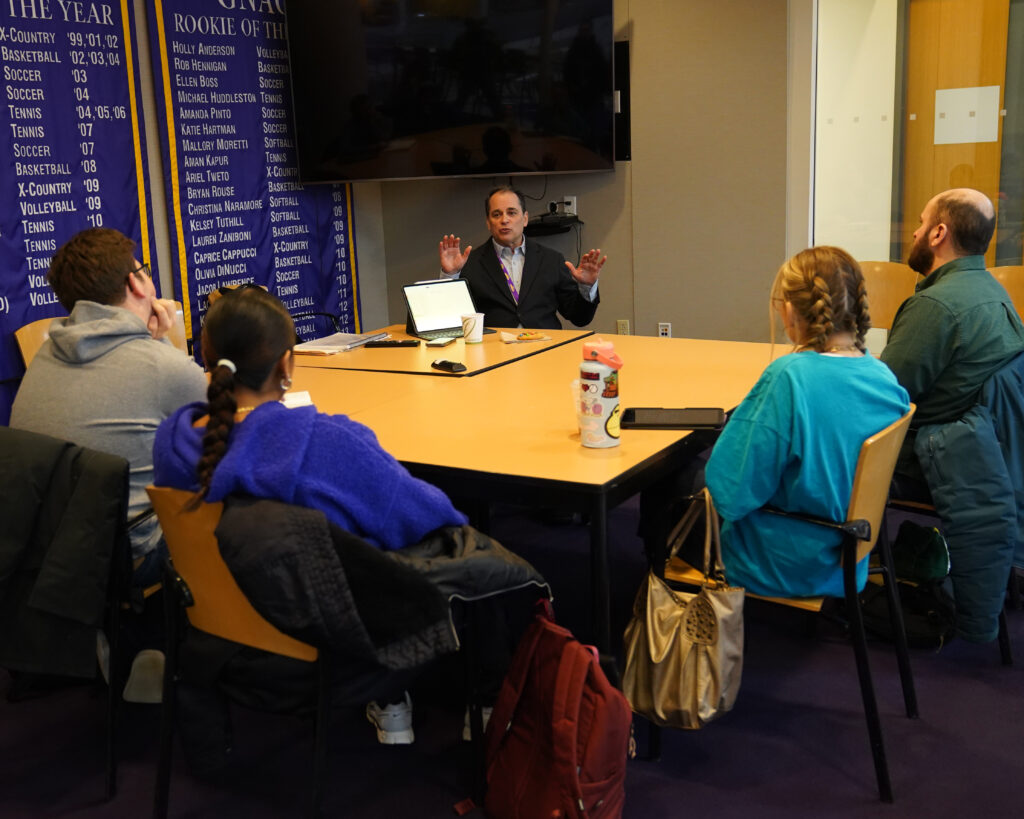 Tim Neverett at a table speaking with people listening and their backs turned to the camera