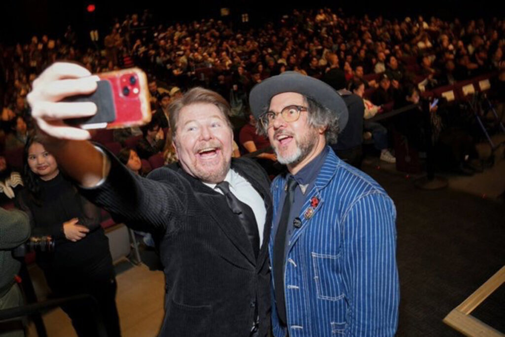 Two men take selfie in front of packed movie theater