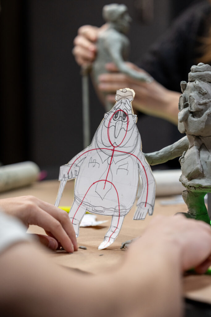 Michael Greene holds a 2D drawing of Wadsworth in his hands while working on his 3D clay mold of the character