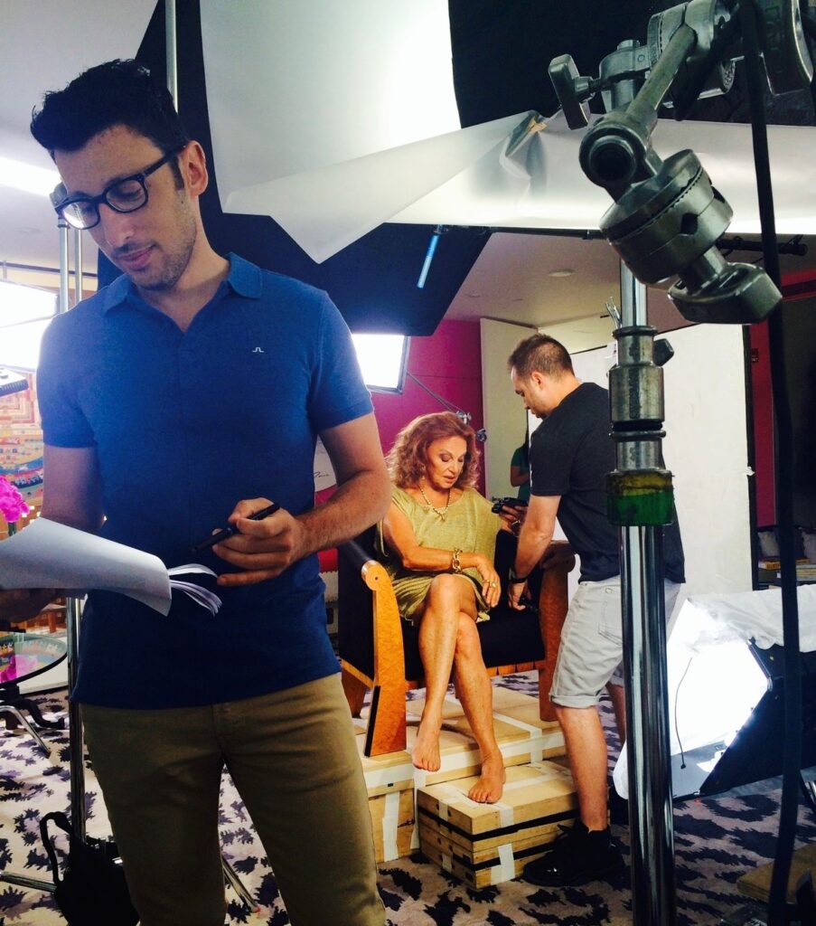 Lenid Rolov in foreground looking at papers while Diane Von Furstenberg sits in a chai in the background working another person working with her