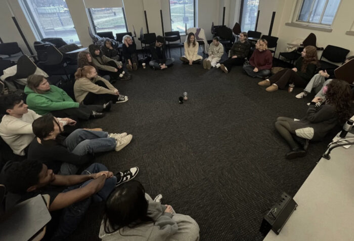 Students sit on the floor in a circle