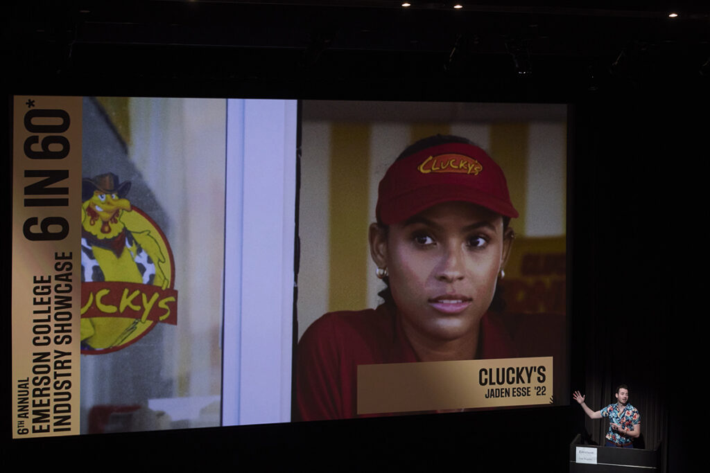 large screen with sill from Clucky's film, filmmaker jaden esse at podium in lower right corner