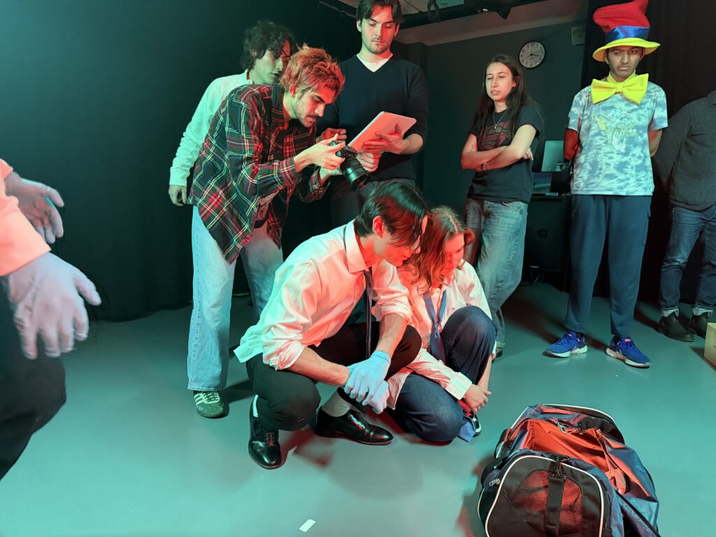 Two people kneel down looking at a bag while someone holds a camera right behind them and other people look on