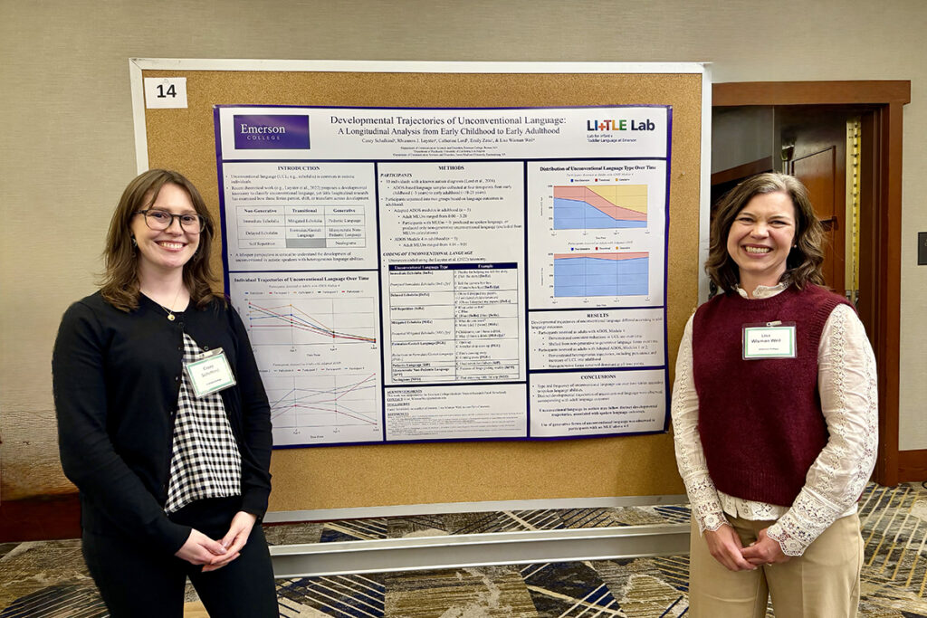 two women stand on either side of a cork board with a research poster pinned to it