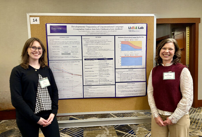 two women stand on either side of a cork board with a research poster pinned to it