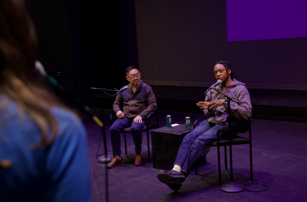Josh Johnson answers a question while sitting in a chair with Ed Lee next to him, and the back of the person answering the question is visible