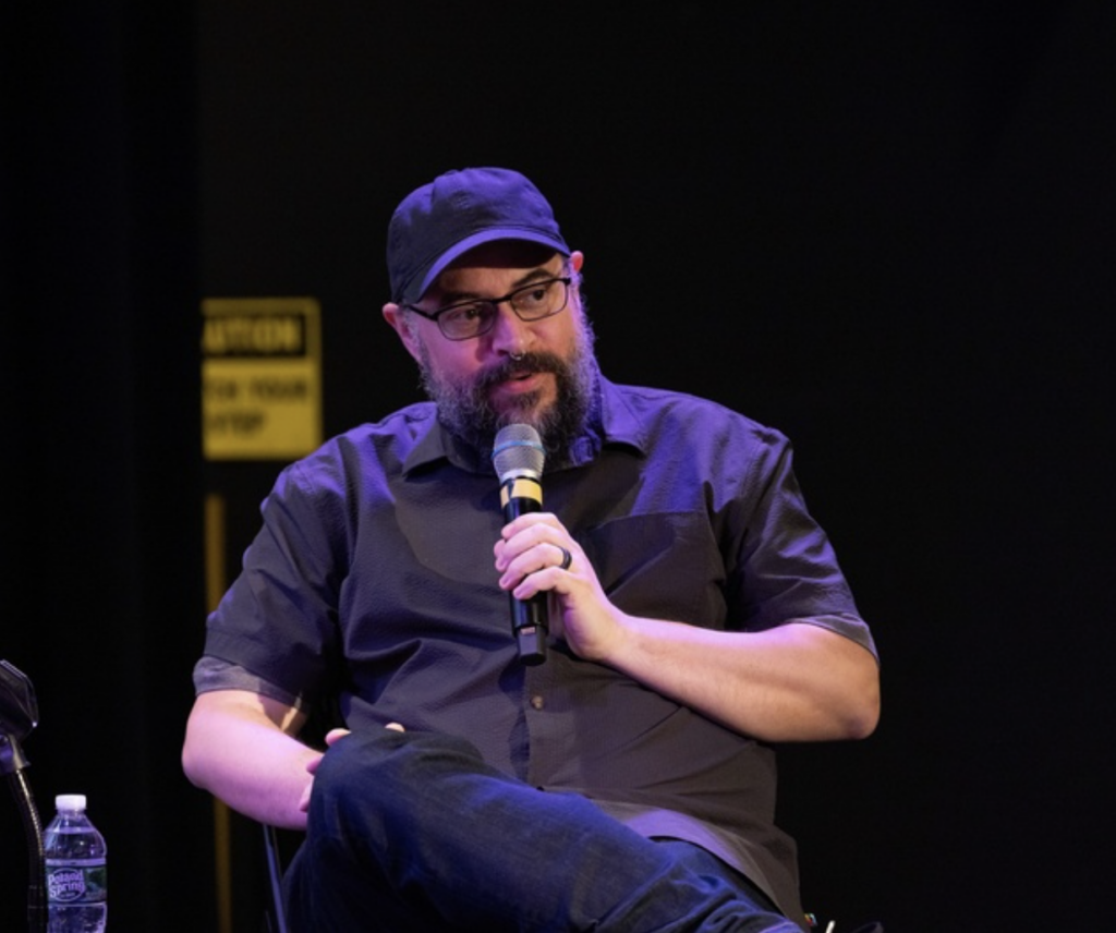 Michael Gilday speaks while holding a microphone and sitting down