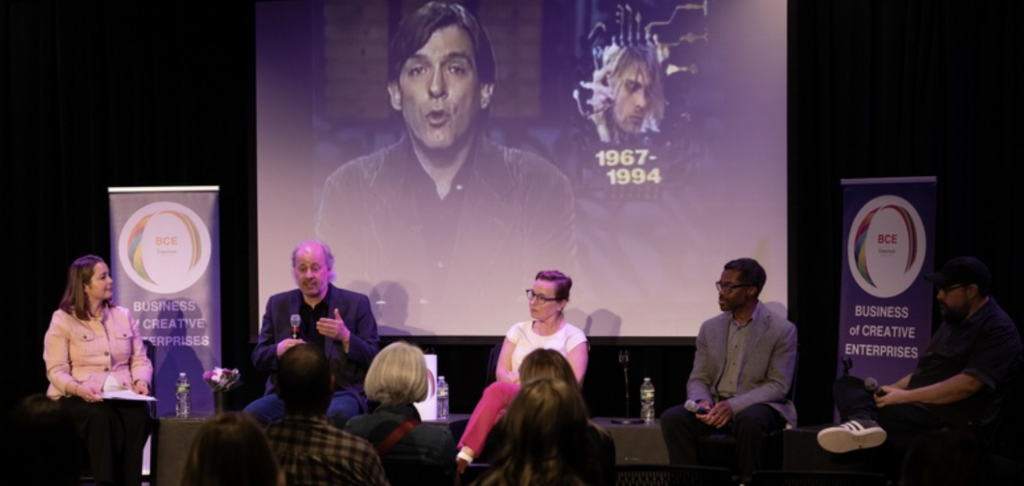 Five people on stage participate in a panel discussion with a projected image behind them.