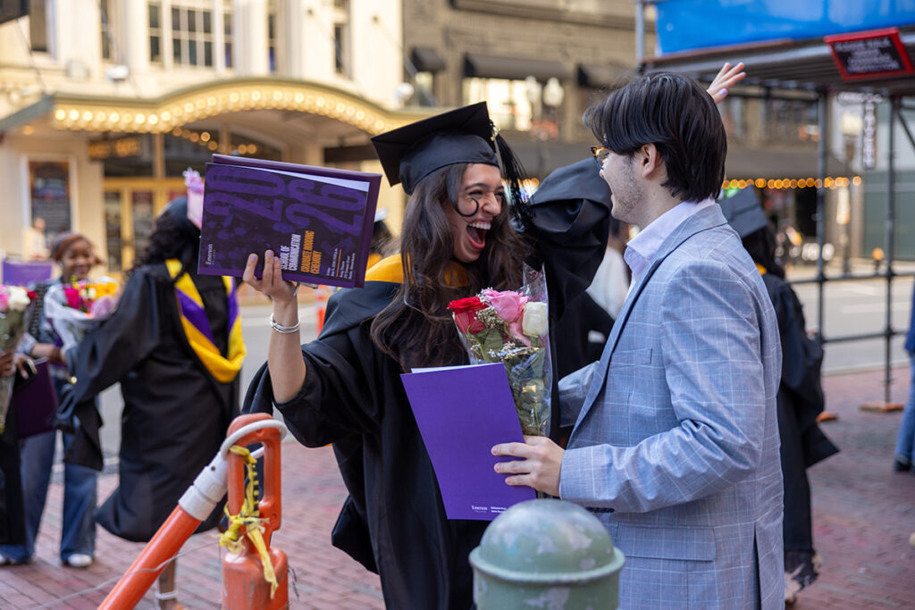 Graduate smiles and goes to hug man holding flowers