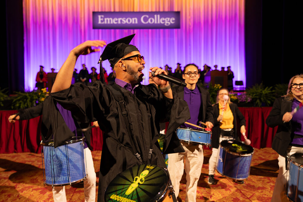 Marcus Santos, in cap and gown holding a drum, speaks into a mic