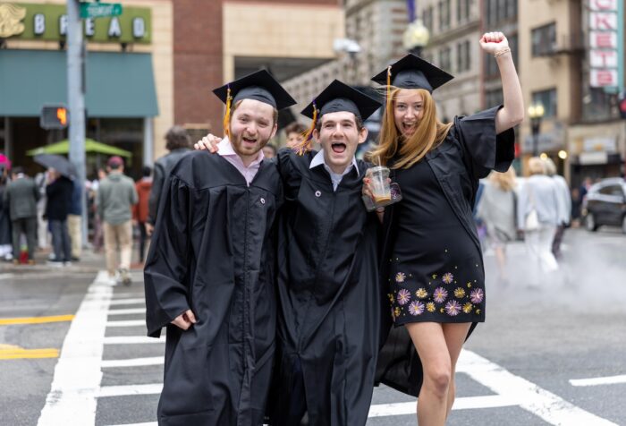 Three students pose in a crosswalk in their caps and gowns