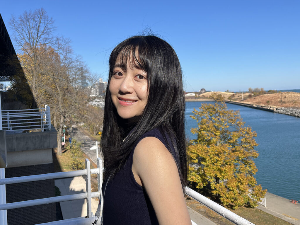 Meng-Hsuan (Amber) Ho leaning against a balcony rail, water in background